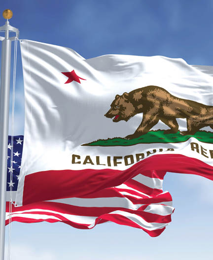 The California state flag flying along with the national flag of the United States of America. In the background there is a clear sky. The flag depicts a walking bear and a five-pointed red star